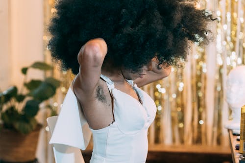 Side view of unrecognizable African American female with Afro and hairy armpits putting on white dress in dressing room