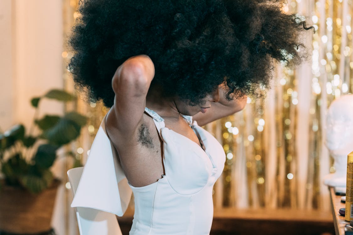 Free Side view of unrecognizable African American female with Afro and hairy armpits putting on white dress in dressing room Stock Photo