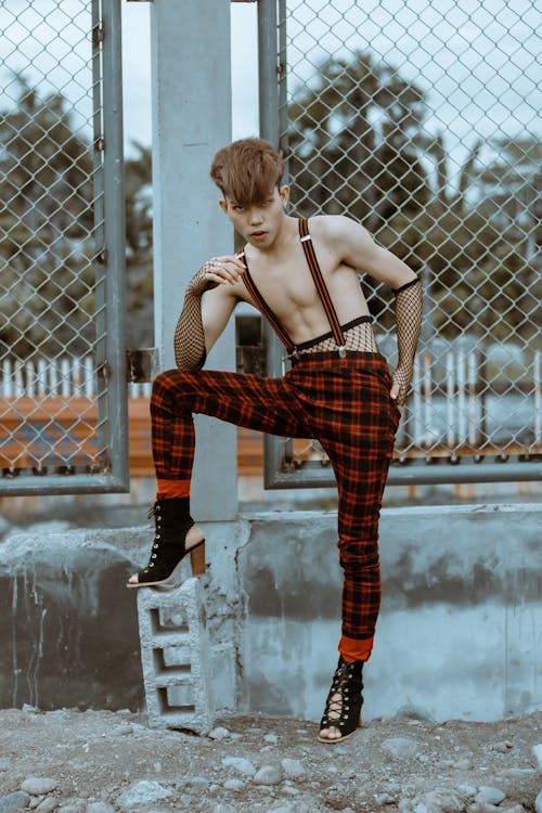 Funky shirtless man in checkered trousers standing near water puddle