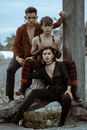 Young extravagant ethnic people in informal clothes sitting together on tree trunk in garden and looking at camera