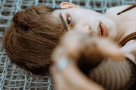 Young shirtless Asian male model in net fingerless gloves outstretching hand and looking at camera while lying on net fence