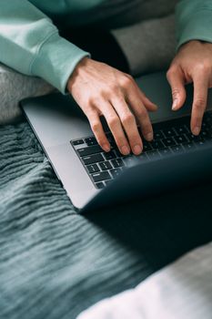 From above crop unrecognizable black person working and typing information on netbook on sofa