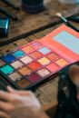 From above kit of eyeshadows of different color in box lying on wooden table near cosmetic brush