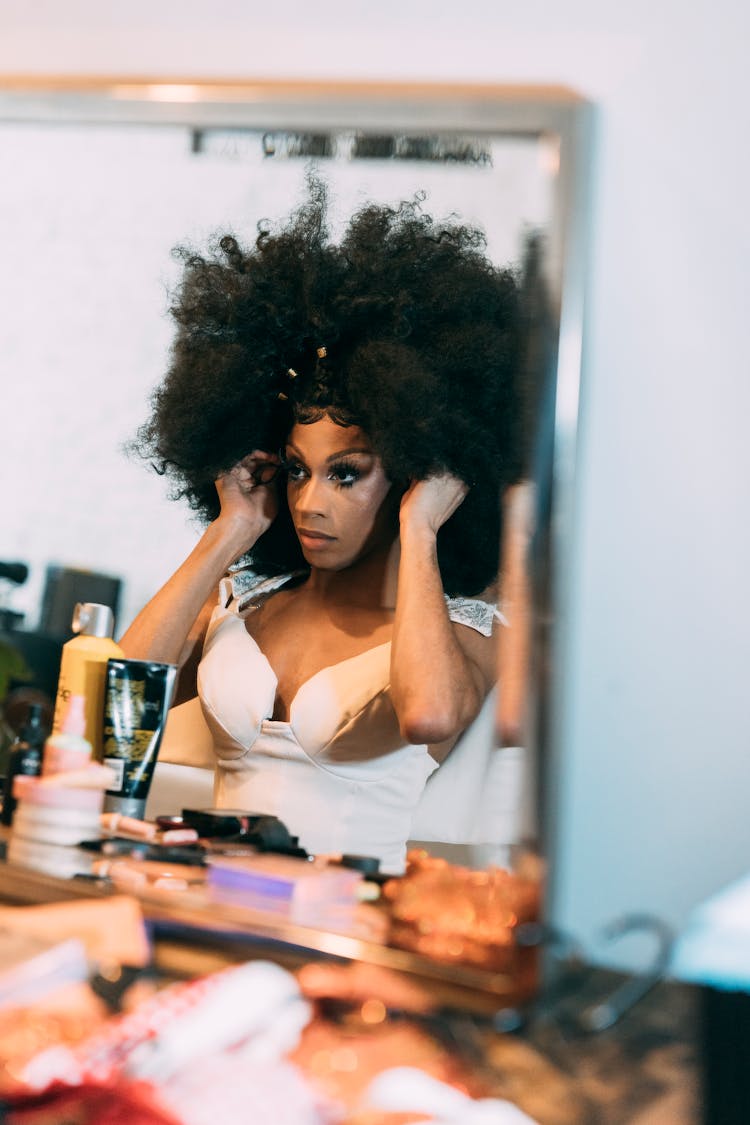 Black Drag Queen Putting On Wig In Front Of Mirror