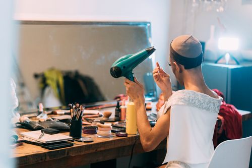 Free Side view of ethnic transgender male sitting in front of mirror and drying hair preparing for show in dressing room Stock Photo