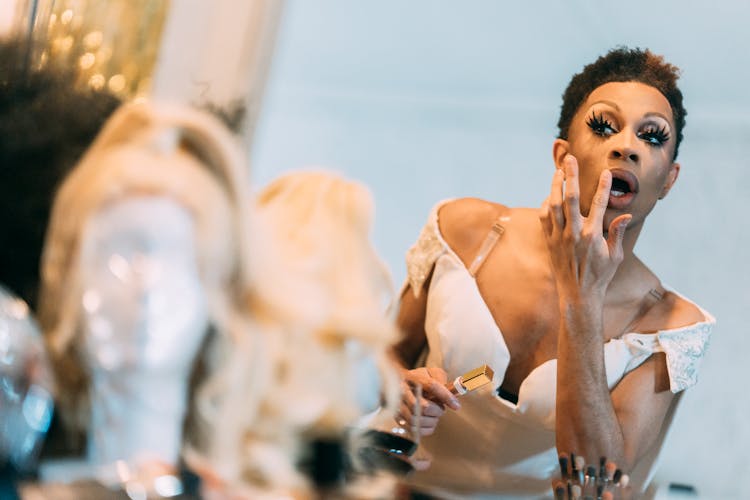 Ethnic Man Applying Lipstick In Front Of Mirror