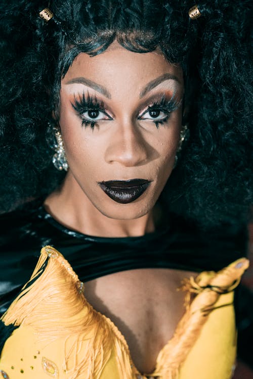 Eccentric African American male drag queen with bright makeup and false lashes wearing wig and stage costume