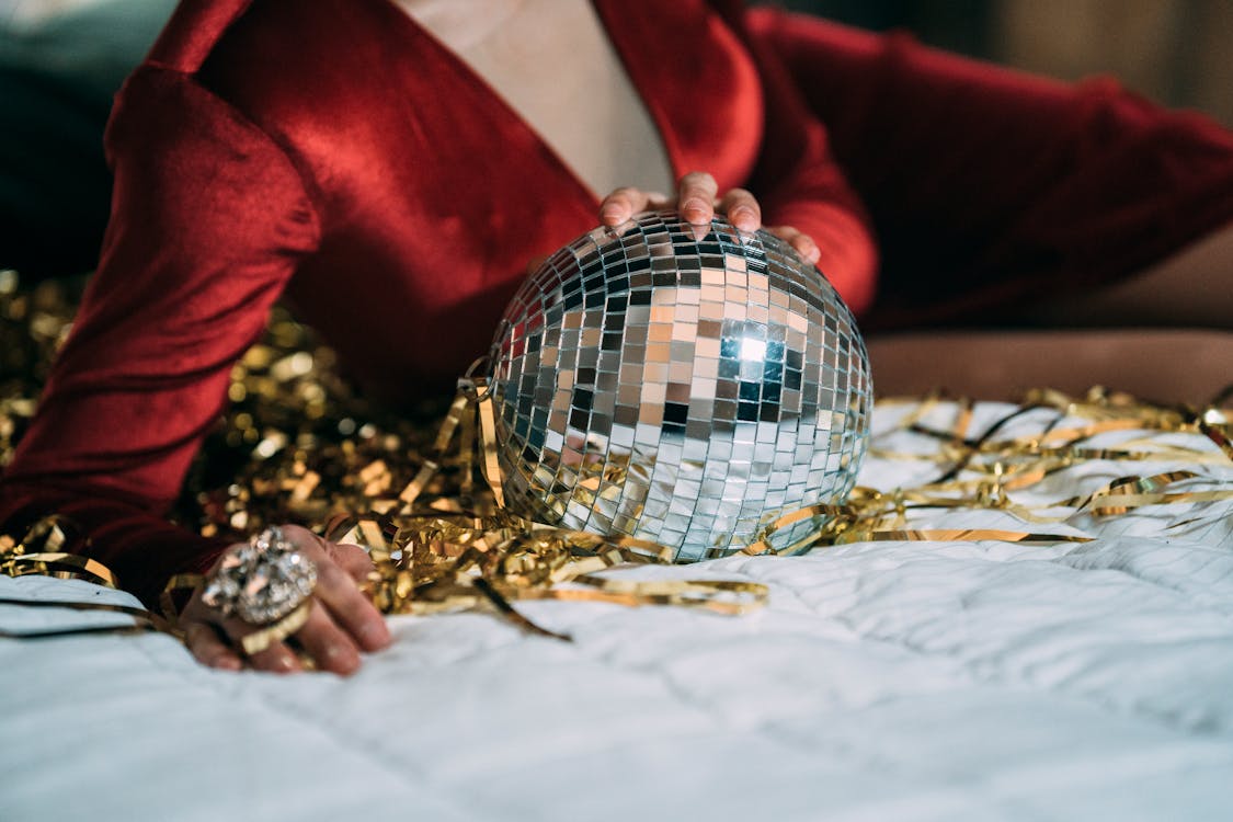 Crop anonymous male in red velvet dress of drag queen lying on bed with glass disco ball
