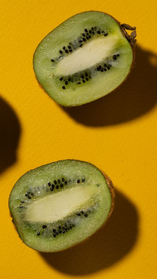 Free Close-up shot of fresh kiwi halves on a vibrant yellow background, highlighting texture and seeds. Stock Photo