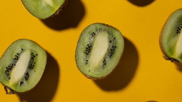 A close-up of fresh kiwi halves placed on a vibrant yellow background showcasing seeds and texture.