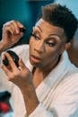 Concentrated black drag queen applying mascara on eyelashes