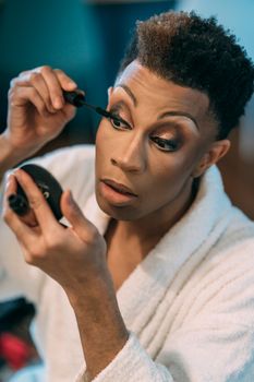 Concentrated black drag queen applying mascara on eyelashes