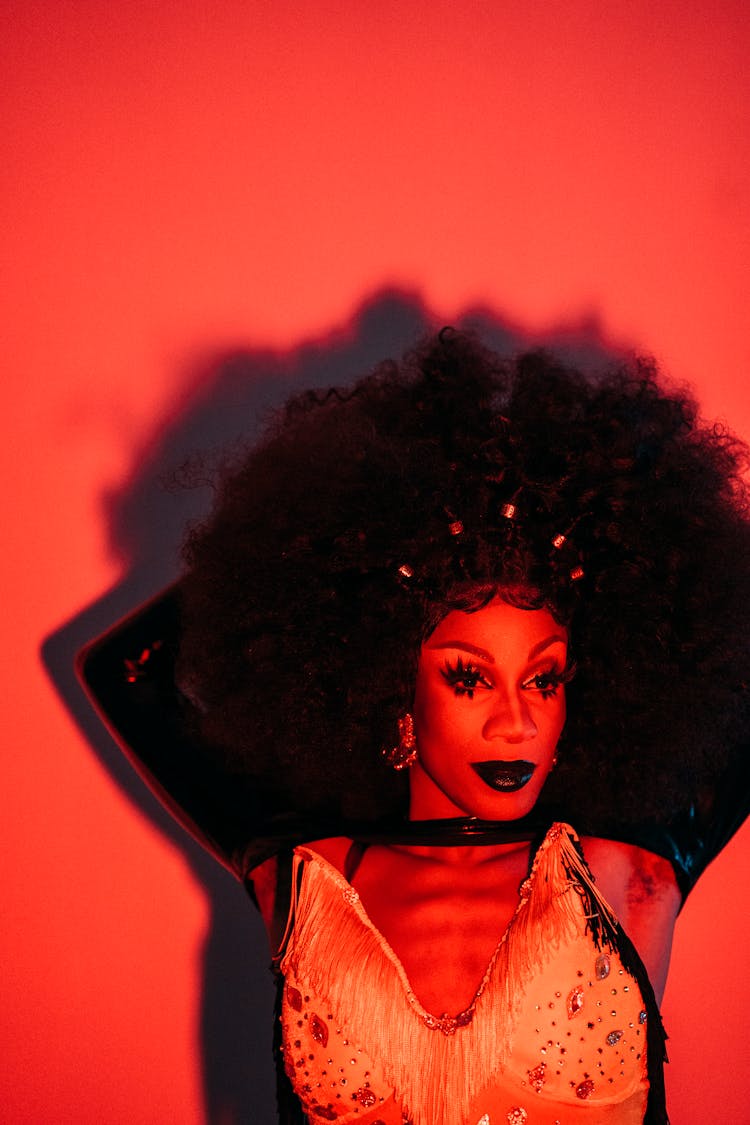 Charismatic Drag Queen Man Standing In Room With Red Light And Looking Away