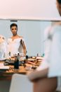 Serious African American drag queen performer with makeup in stylish clothes standing and looking at mirror in light dressing room