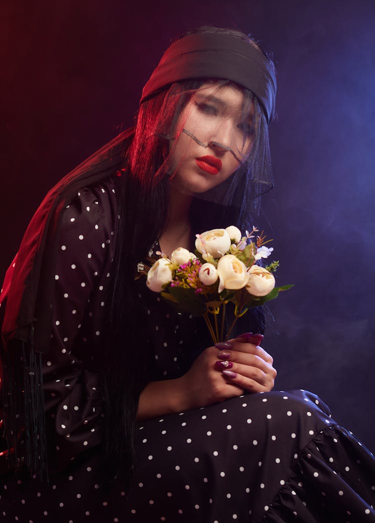 A Woman Wearing Black Dress And Veil Holding A Bunch Of Flowers