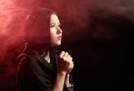 A Woman in Black Top Praying in a Room with Smoke