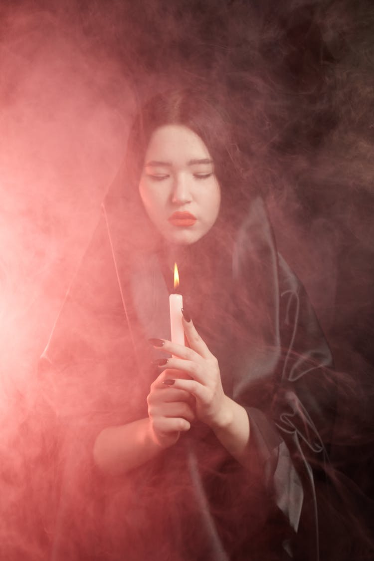 A Woman Holding Lighted Candle In A Smokey Dark Room