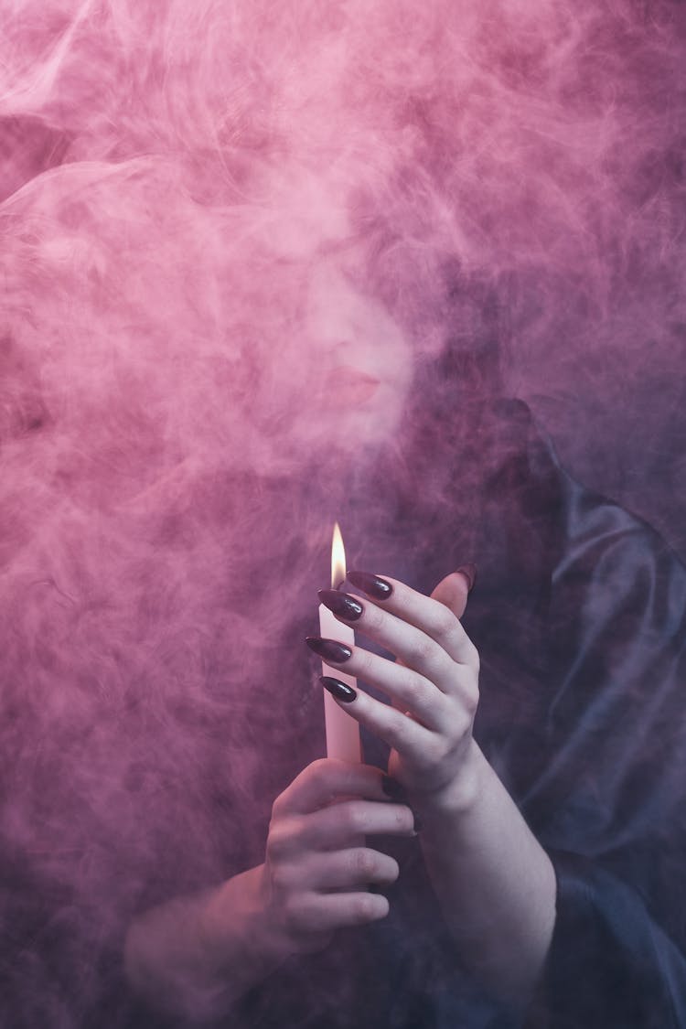 A Person Holding Lighted Candle In A Smokey Dark Room
