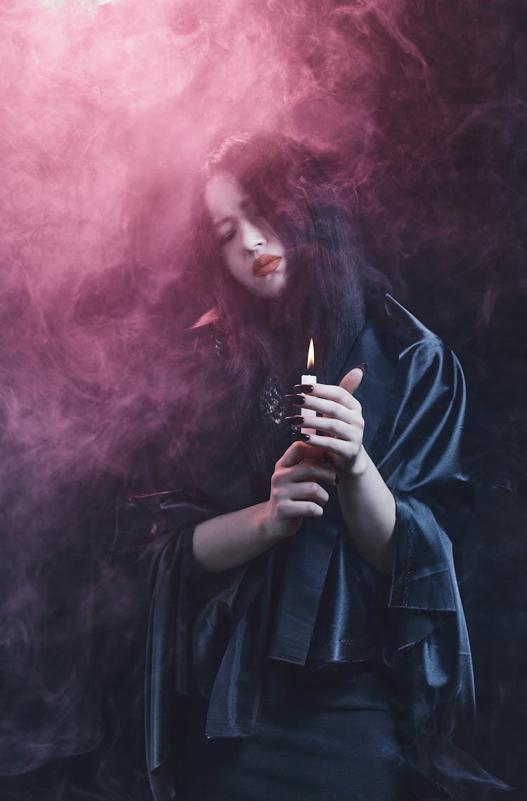 A Woman Holding Lighted Candle In A Smokey Dark Room
