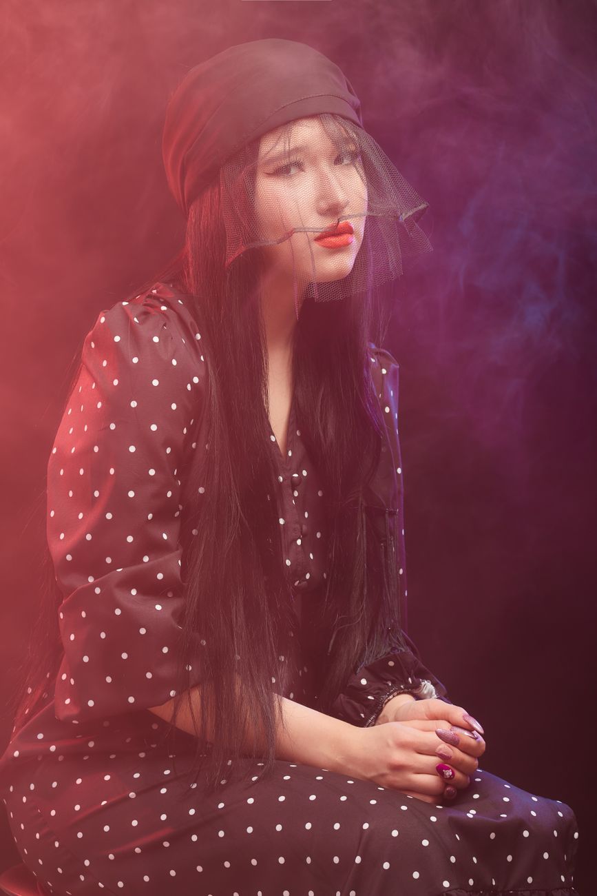 Portrait of an elegant woman wearing a polka dot dress and veil, exuding a moody and artistic vibe.