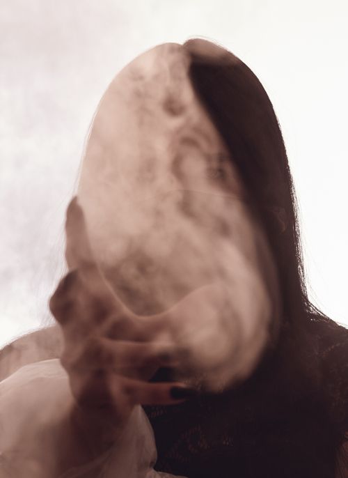 Free A mysterious black and white portrait with smoke obscuring a woman's face, creating an ethereal effect. Stock Photo