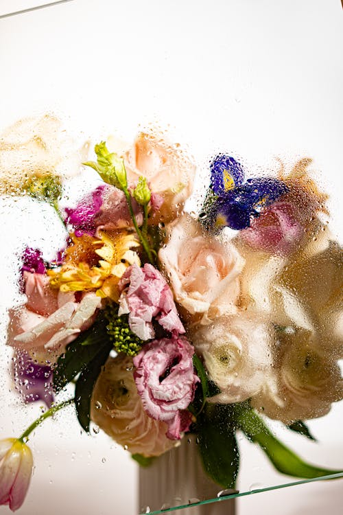 A Vase with Colorful Flowers Behind Moist Glass