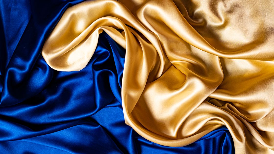 Người thợ đang kiểm tra và so sánh ba loại vải lụa áo dài trên bàn cắt sáng