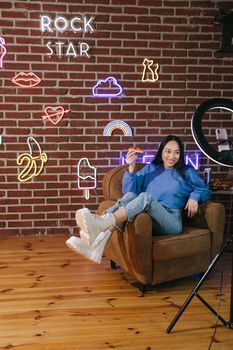 Stylish woman with pizza in vibrant room setting up vlog content.