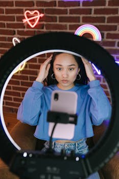 Asian woman recording a video with a smartphone and ring light for streaming purposes.