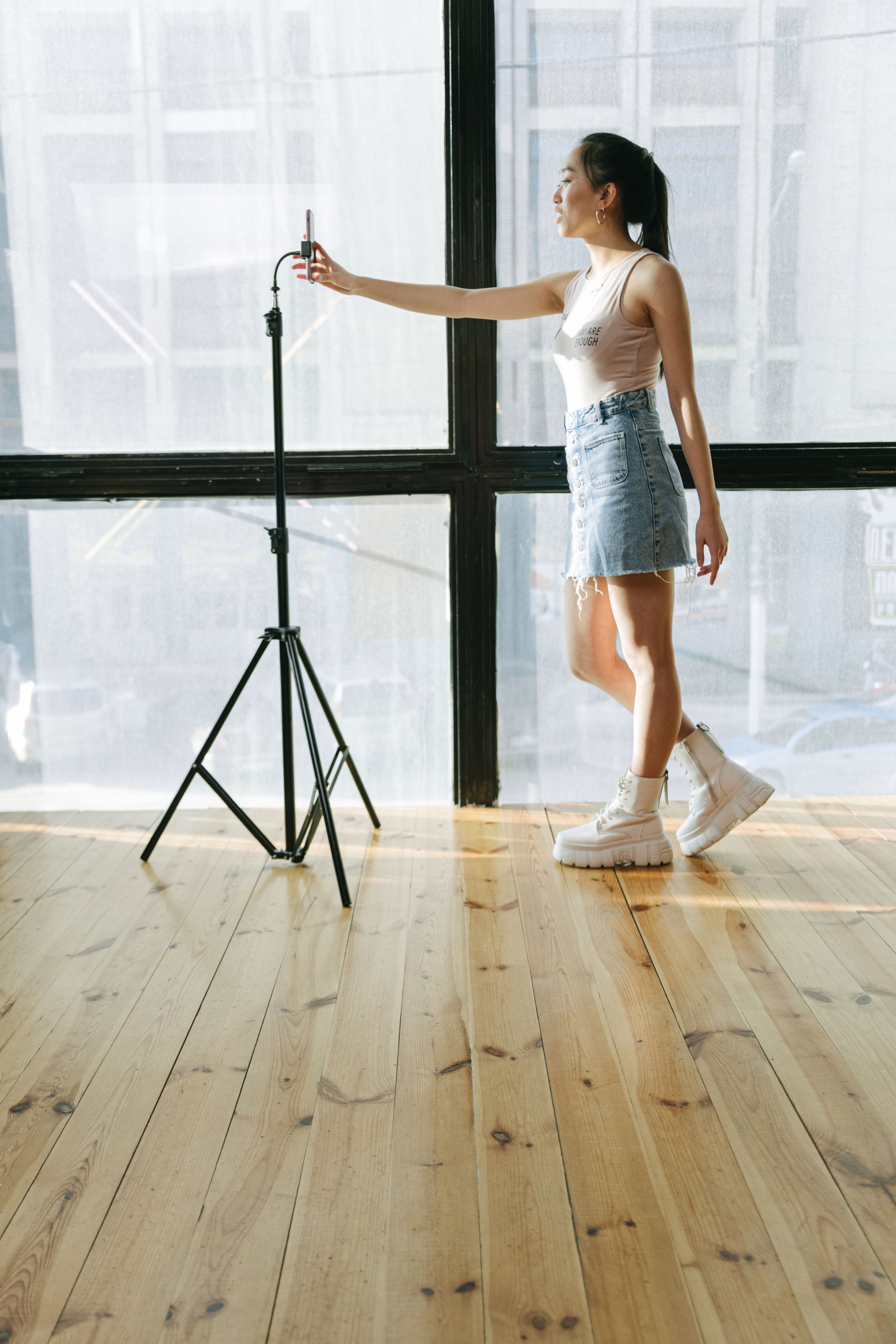 Woman adjusts smartphone on a tripod in a bright space preparing for video filming