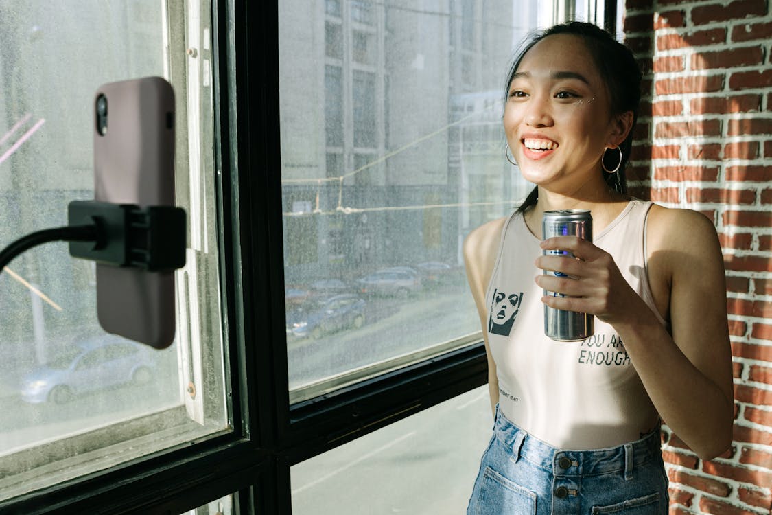 A woman holding a can in front of a smartphone filming a TikTok.