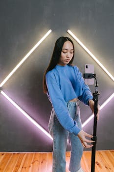 Teen influencer adjusting smartphone on tripod with neon lights in the background.
