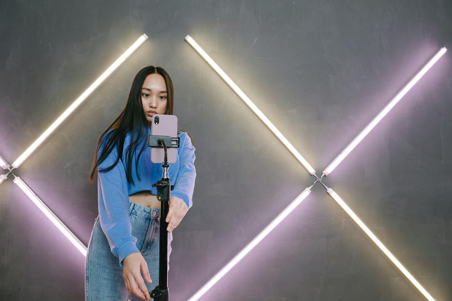 Teen girl taking a selfie with a tripod in front of a neon-lit wall, creating a modern influencer vibe.