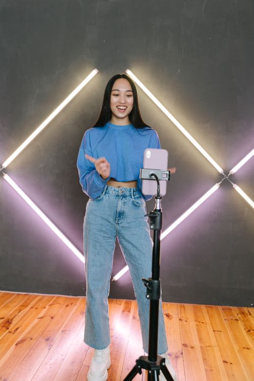 Free Asian woman vlogging with a phone on tripod in stylish room with geometric lighting. Stock Photo
