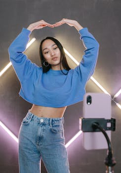 Teenage influencer demonstrates dance moves in front of neon lights, filmed with a smartphone.