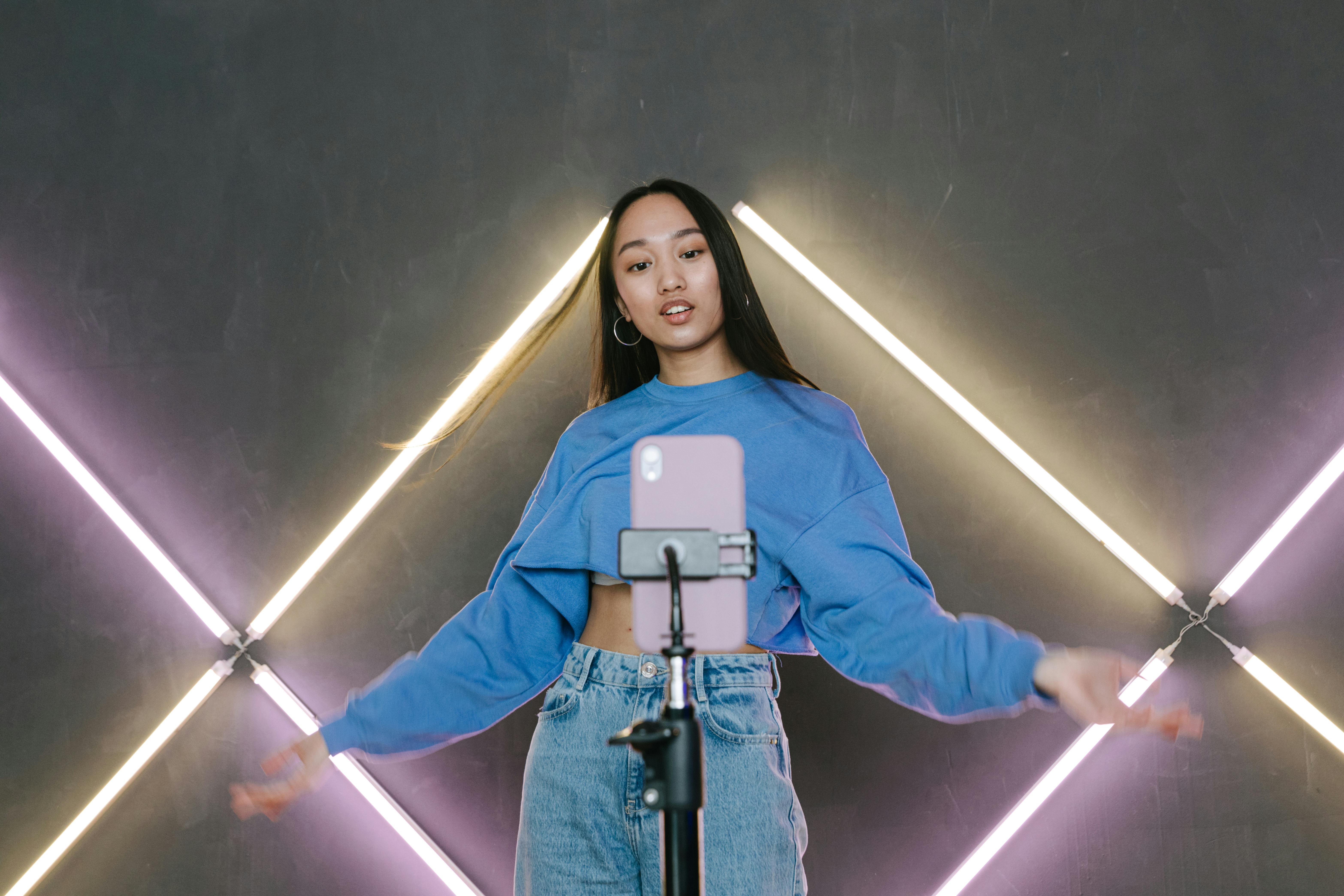 a woman in blue sweater dancing in front of her mobile phone on a tripod