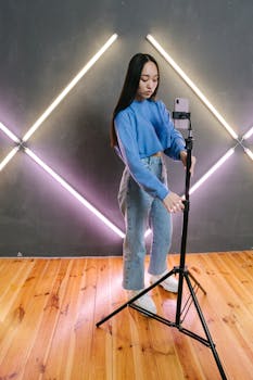 Asian woman adjusts smartphone on tripod in modern studio for content creation.