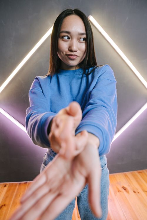 Free A young woman in a blue sweater poses playfully indoors with neon lights in the background. Stock Photo