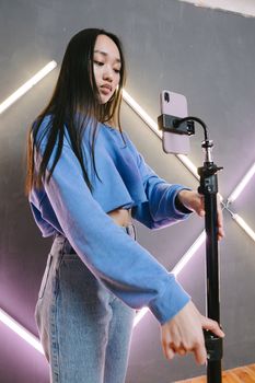 Young woman in blue sweater using smartphone tripod indoors.