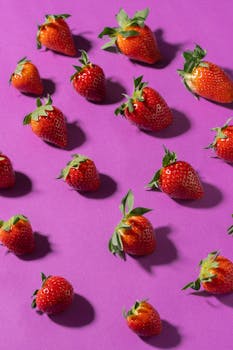 Ripe strawberries scattered on a purple background, showcasing a fresh and colorful composition.
