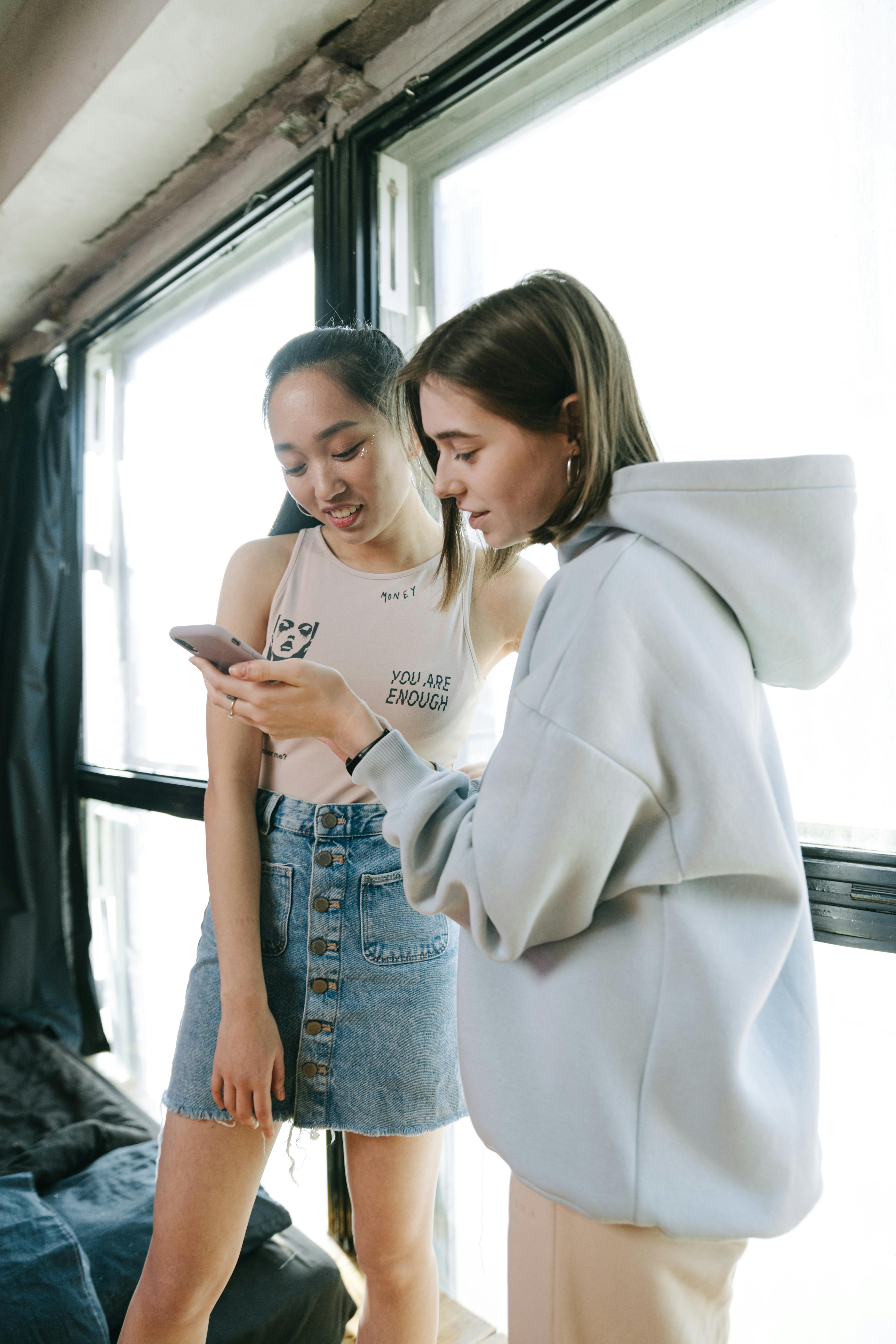 Two young women looking at a smartphone together in a bright room, sharing a moment.
