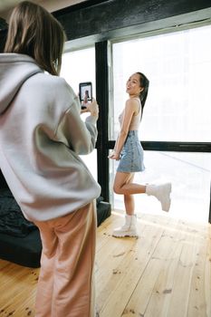Woman in casual outfit being recorded by friend with smartphone, showcasing modern lifestyle.