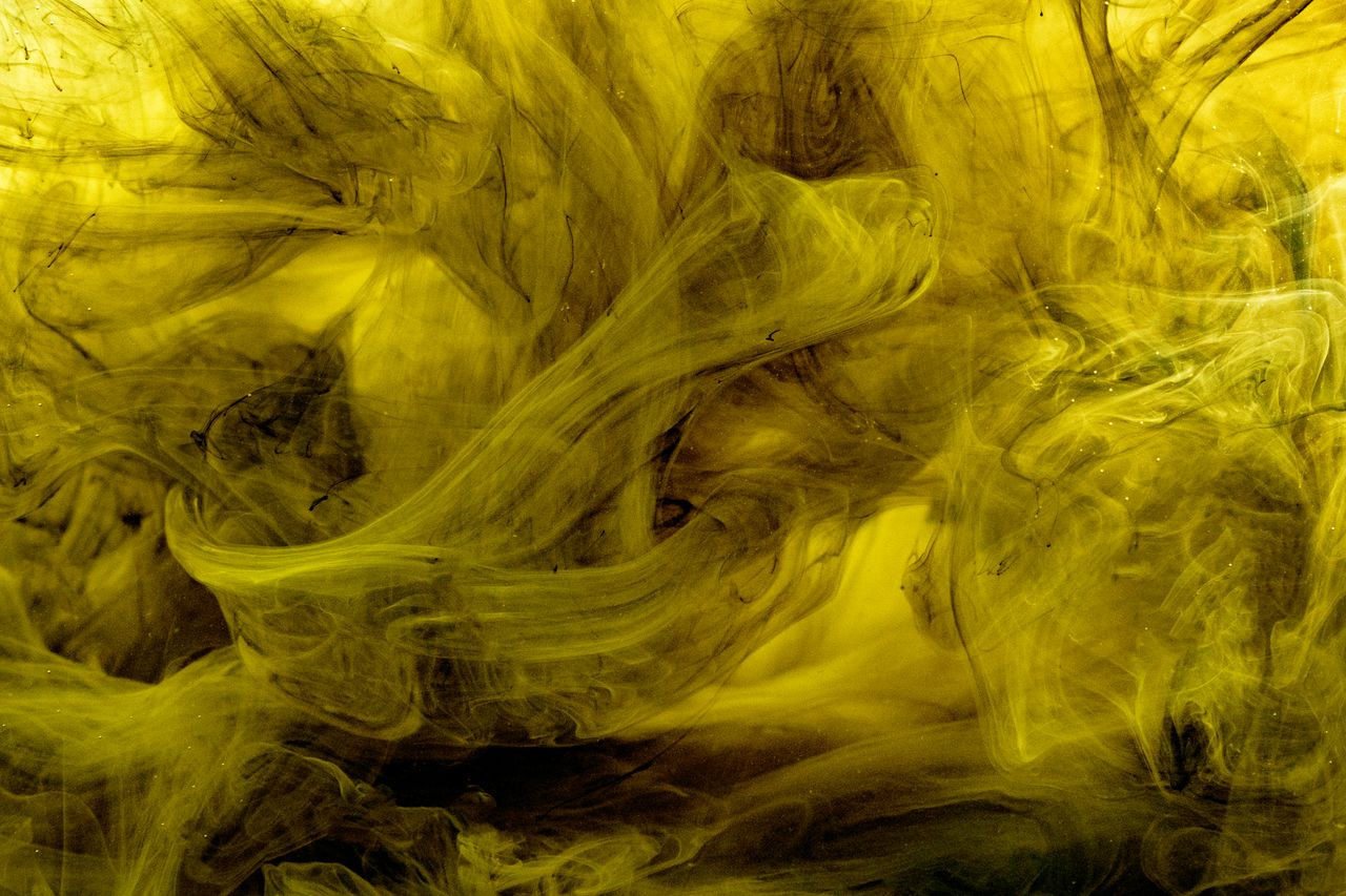 abstract artistic capture of yellow ink swirling in liquid creating a