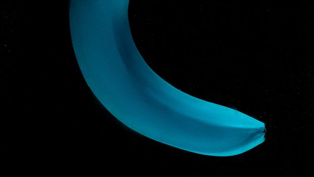 A close-up of a banana painted blue against a black background, abstract and conceptual.