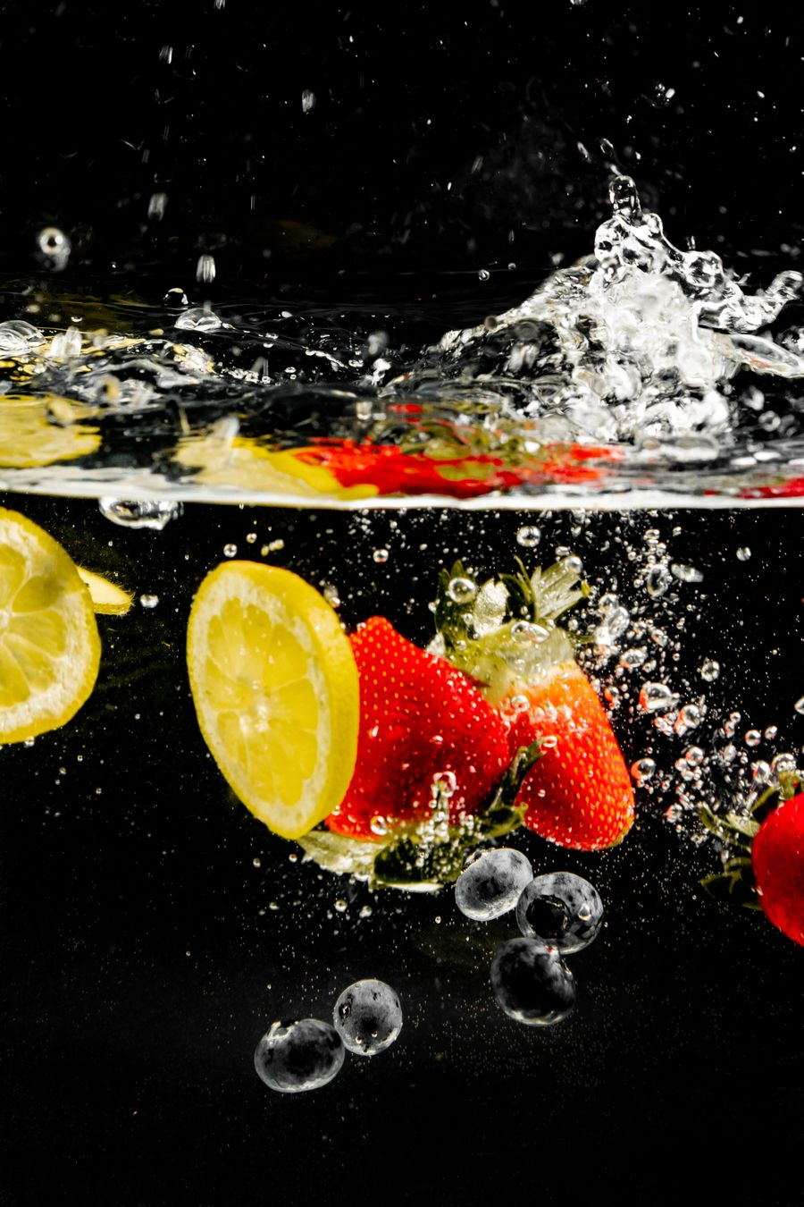 Lemons, strawberries and blueberries splashing in water with bubbles