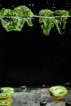 Vibrant broccoli and kiwi submerged in water with a dark background, showcasing freshness.