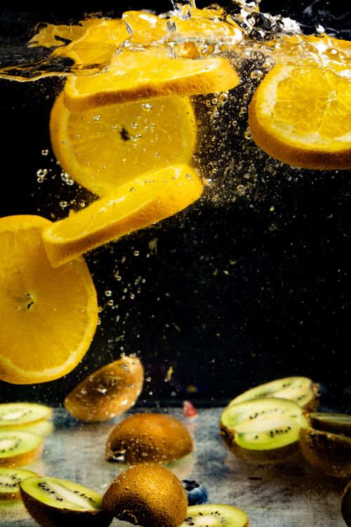 Free Refreshing splash of orange and kiwi slices in clear water on a dark background, capturing motion and freshness. Stock Photo