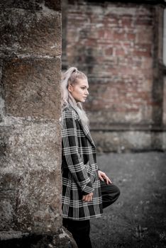 Woman in a plaid coat leaning against a stone wall outdoors in Charfield, UK.