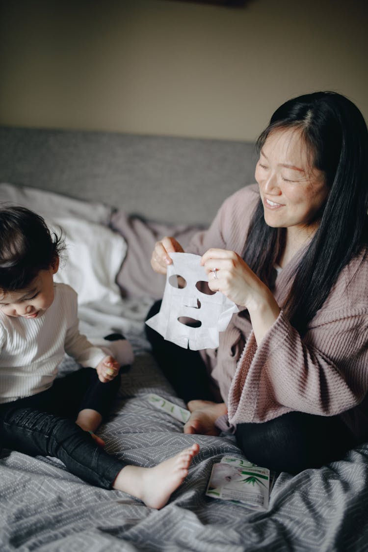 Woman Sitting On Bed Making A Mask Beside Her Child