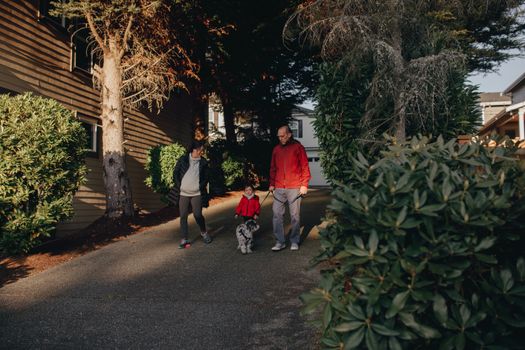 A family enjoys a walk with their pet dog on a sunny day, surrounded by lush greenery in a suburban neighborhood.